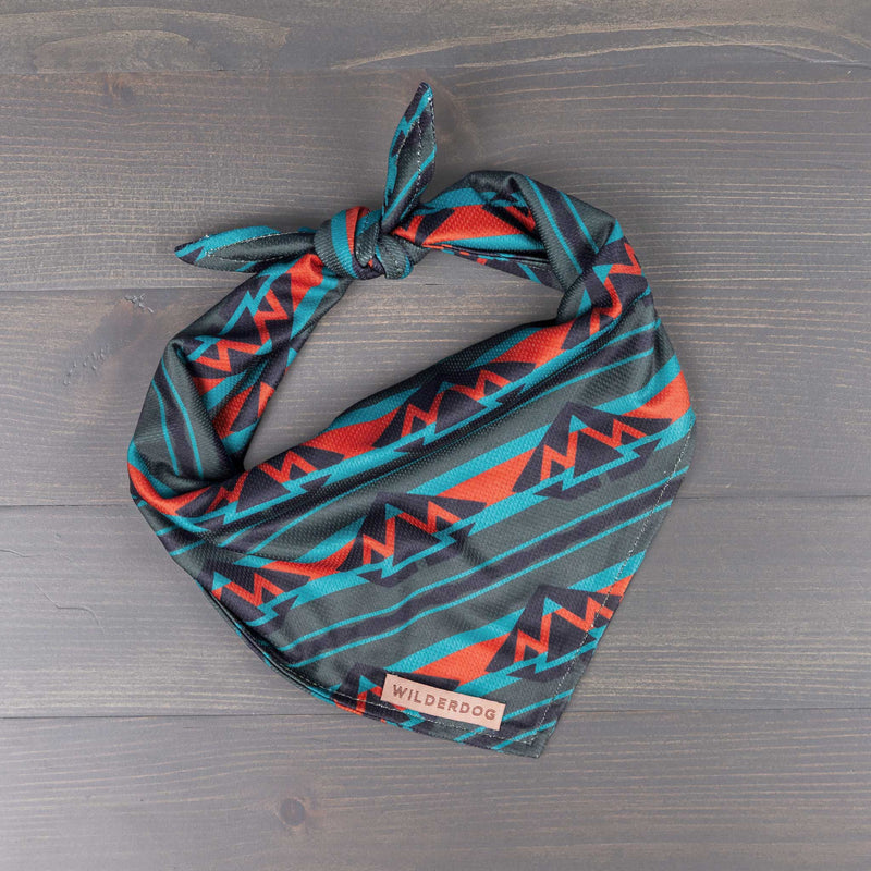 Olive Bandana with abstract mountain pattern in teal, red, and black, tied and displayed on wood.