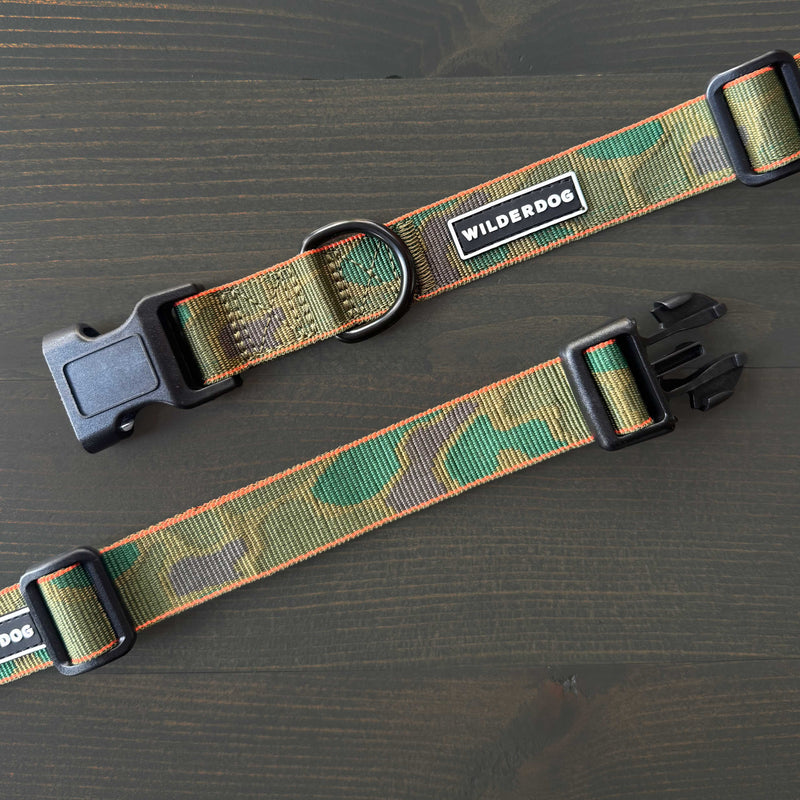 Two "Camo Ultralight Collar" dog collars in green camouflage nylon, featuring black plastic buckles and metal rings with Smartcart21 branding, are displayed on a dark wooden surface.