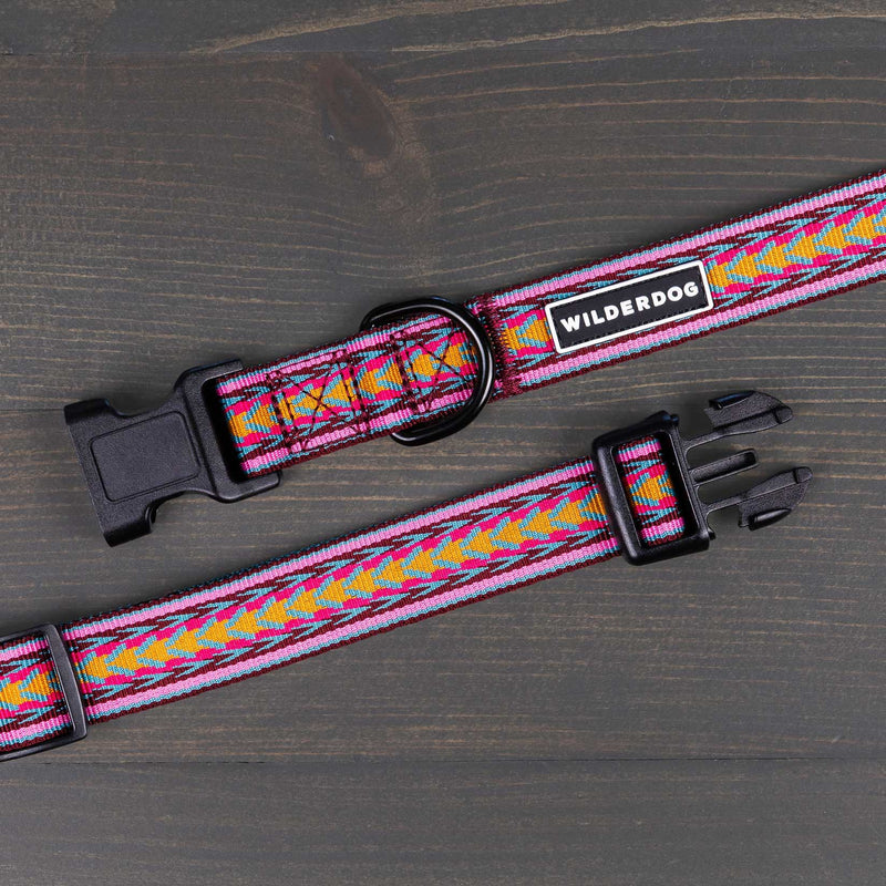 A vibrant Daybreak Ultralight Collar showcases a multicolored geometric pattern set against a gray wooden background. This nylon webbing collar is fitted with a black plastic side-release buckle and a D-ring, and prominently features the "Wilderdog" brand label.