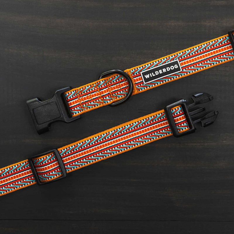 Displayed is the Sienna Ultralight Collar from the Ultralight Collection, showcasing a vibrant, woven design featuring red, orange, white, and blue patterns. The nylon webbing collar includes a black plastic buckle, D-ring, and adjustable strap. A tag reading "Wilderdog" brands the collar. The background is a dark surface.