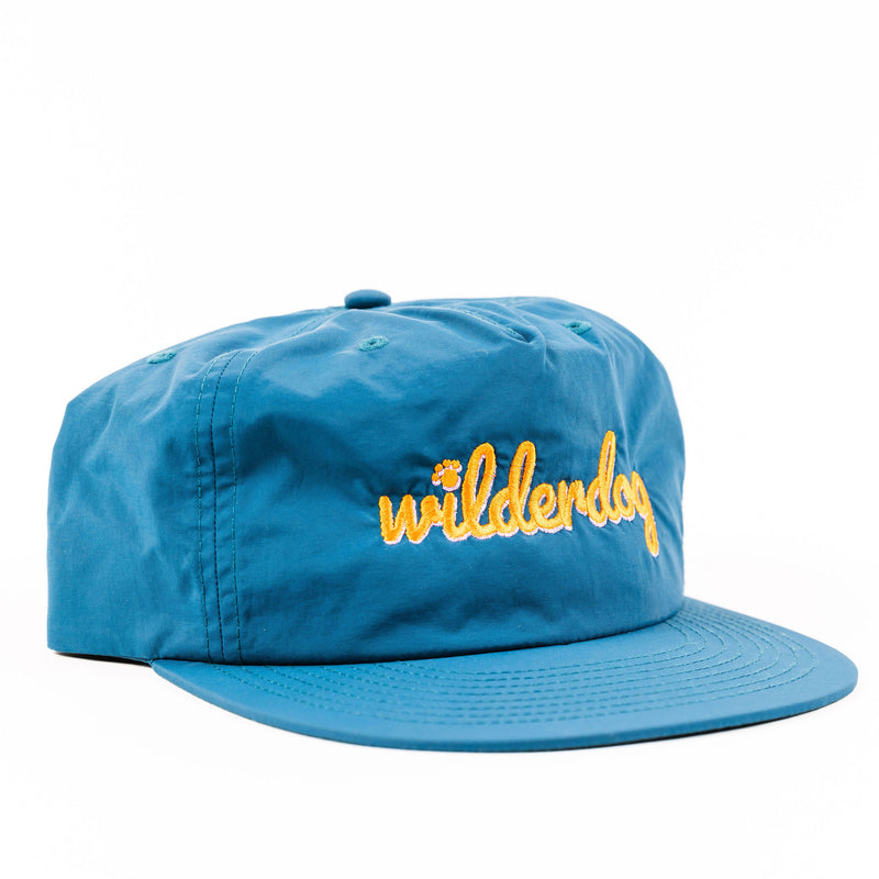 The Smartcart21 Surf Hat is a lightweight, quick-dry, blue snapback cap made from recycled nylon, featuring "wilderdog" embroidered in yellow cursive lettering across the front. It is displayed at an angle against a white background, showcasing both the front and part of the side - perfect for any adventure.