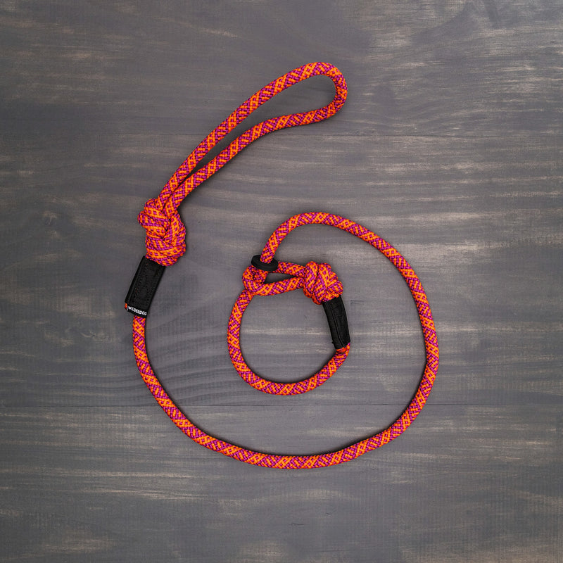 The Sierra Slip Lead, a brightly colored red and orange braided slip lead made from durable rock climbing rope with a loop handle and slip knot collar, is laying on a wooden surface.
