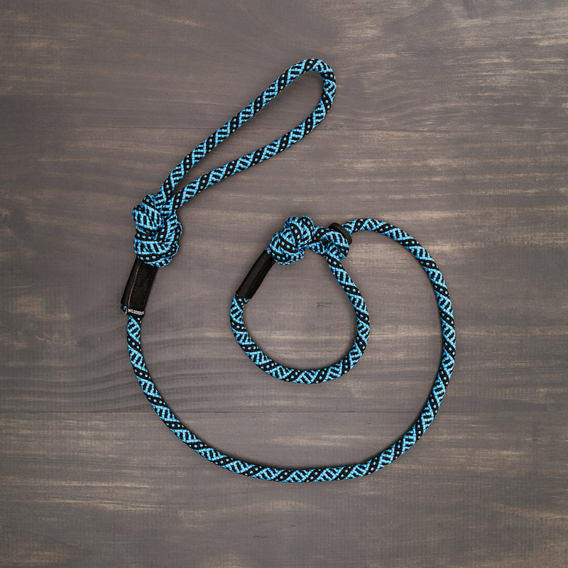 The Teton Slip Lead, a durable rock climbing rope with blue and black strands, featuring a loop at one end and a knot in the middle, is arranged on a dark wooden surface. This rope even comes with a lifetime warranty for your peace of mind.