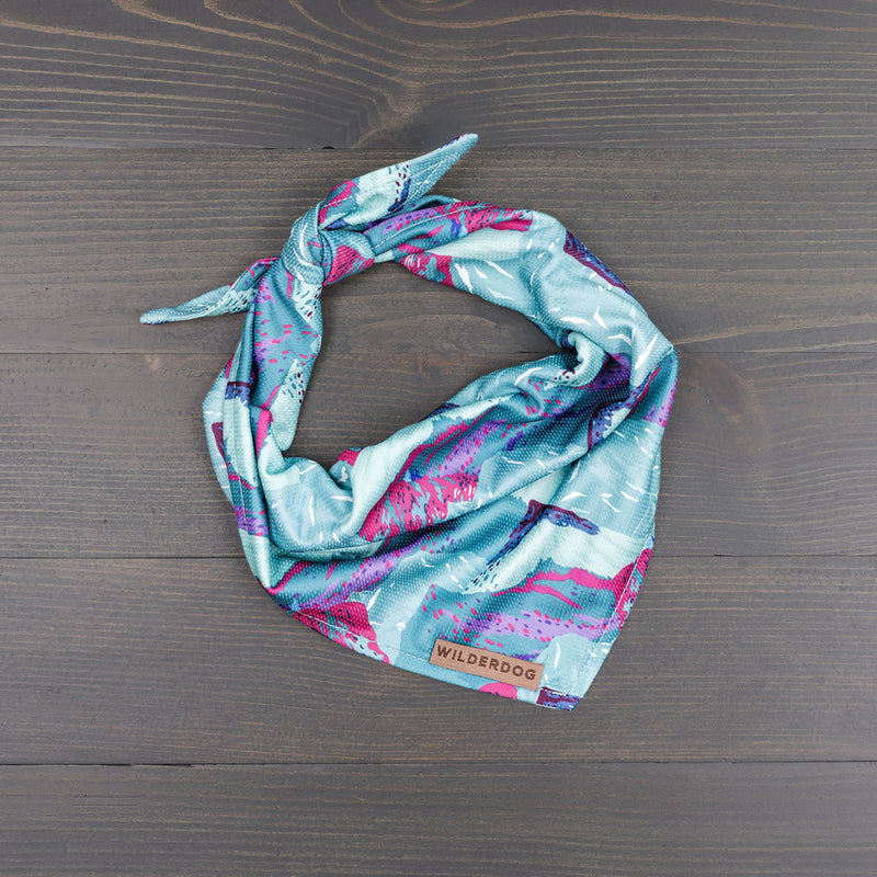 Alpenglow Bandana with teal, pink, and white patterns on wood. Quick-dry mesh.