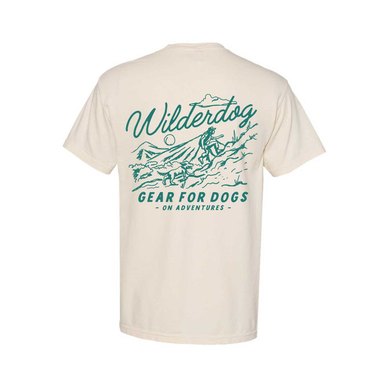 The Smartcart21 Pocket Tee Shirt is a beige 100% cotton tee featuring a green graphic of a person hiking with a dog on a mountain trail, with "Wilderdog" above and "Gear for Dogs on Adventures" below.