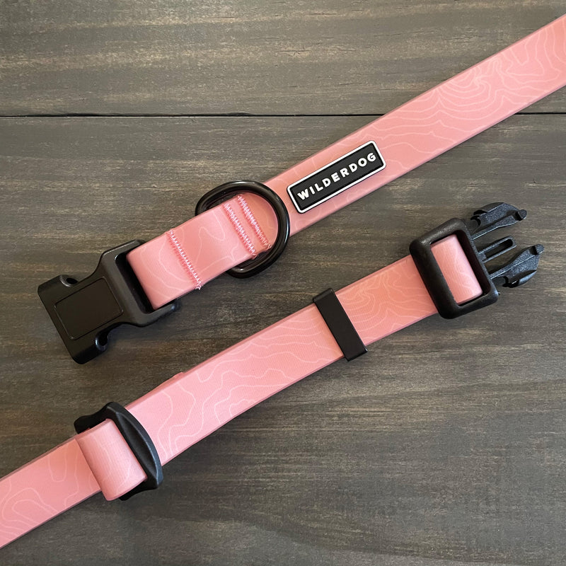 Two pink Guava Waterproof Leash + Collar Bundles with black hardware and a topographic map pattern are displayed on a dark wooden surface, reflecting the brand’s durable dog gear design.