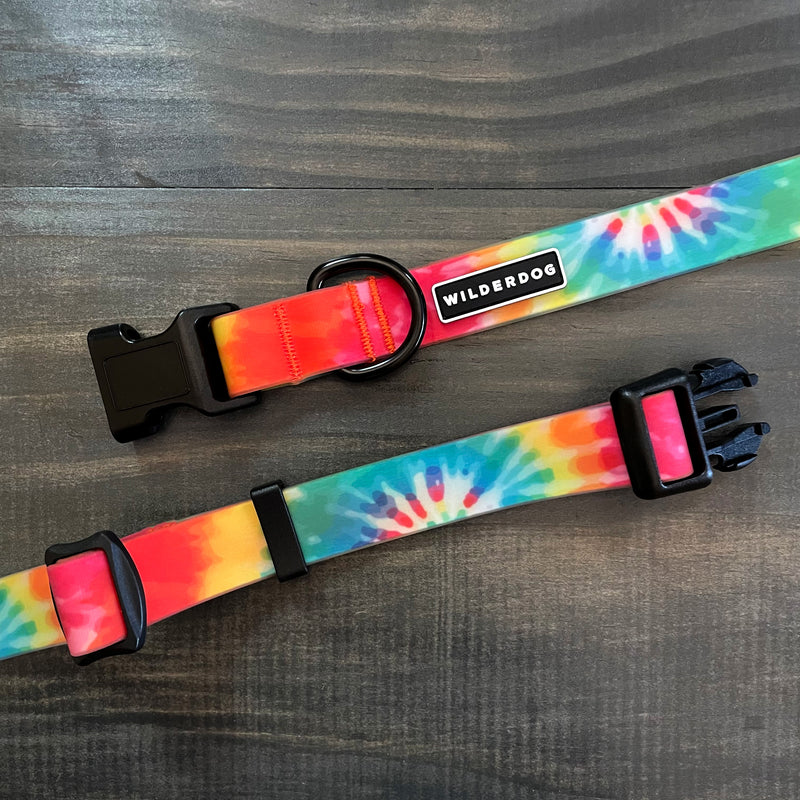 The Tie Dye Waterproof Leash + Collar Bundle features two vibrant dog collars with black buckles and "WILDERDOG" labels, shown on a wooden surface—durable, waterproof gear for adventurous pups.