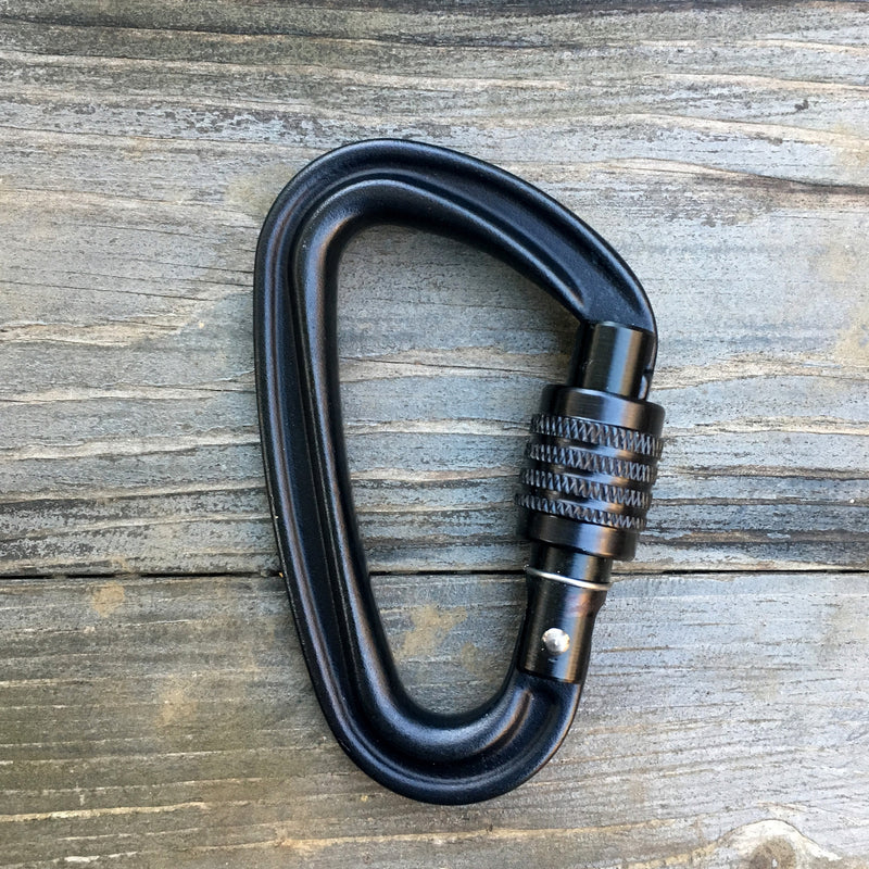 Black carabiner with screw-lock on wooden surface, ideal for climbing and securing during adventures